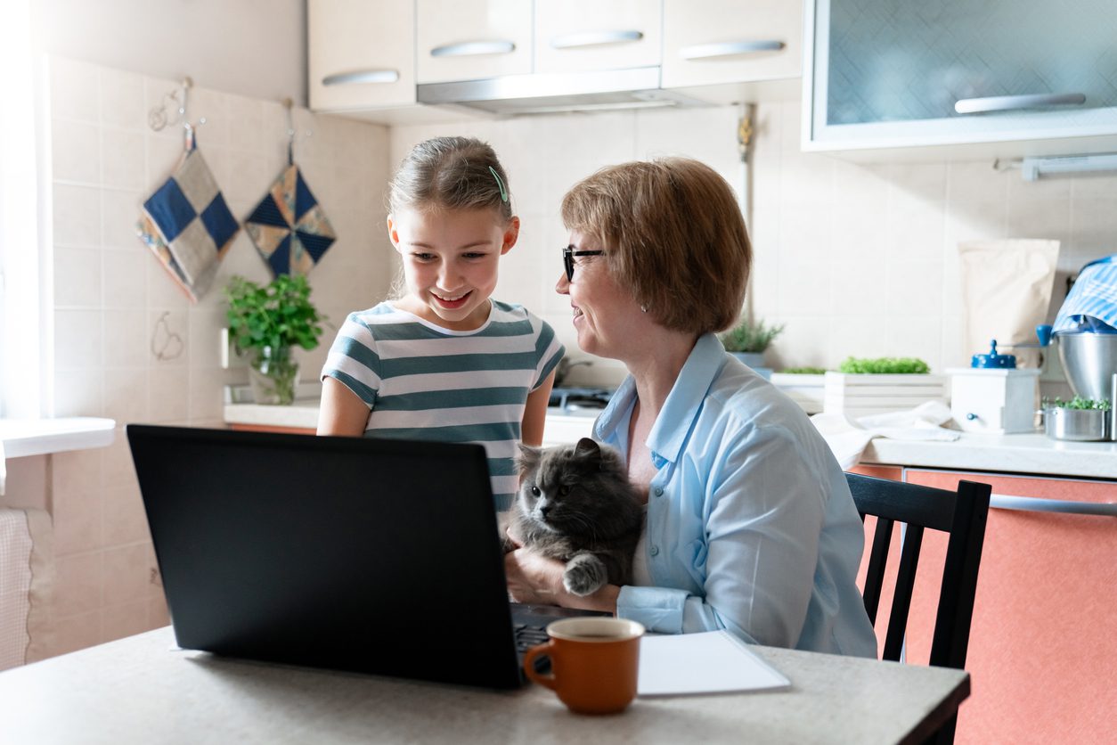 Family using laptop at home. Working mother and daughter. Technology lifestyle, distance education. Woman, child and cat have fun together.